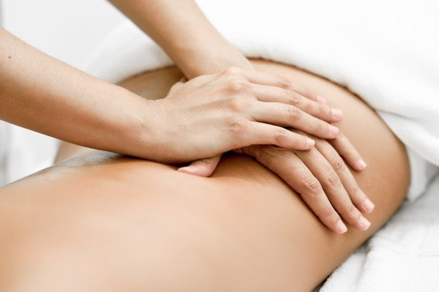 Fizioterapeut drži položene dlanove na leđima pacijenta i radi duboko-tkivnu medicinsku masažu za išijas. 