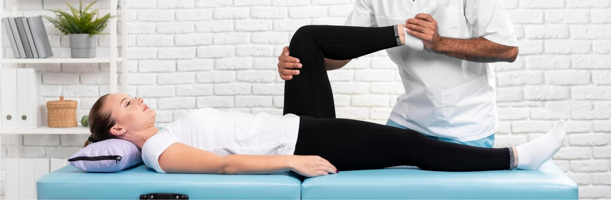Fizioterapeut rukama drži koljeno mlade žene koja leži na krevetu. 