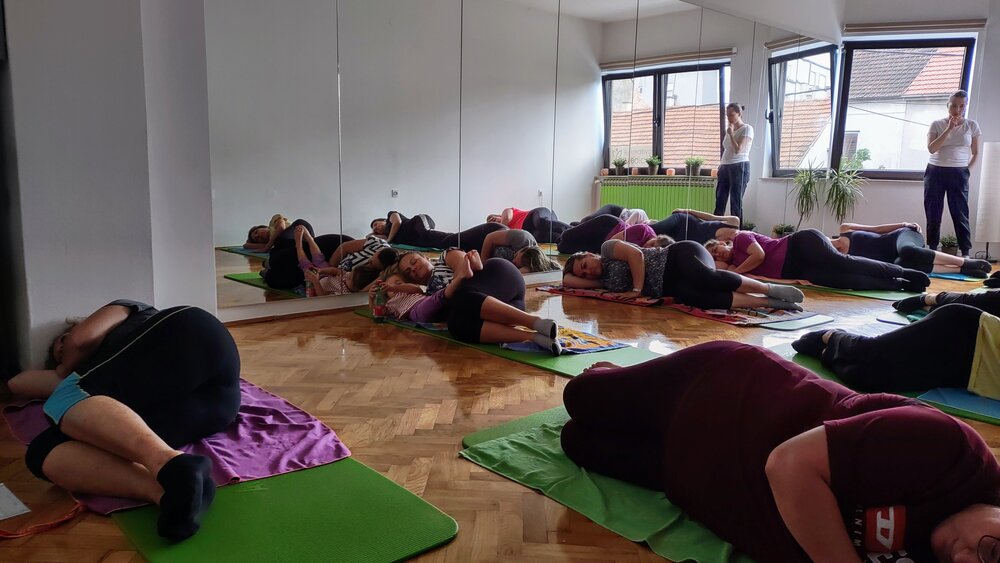Grupa muškaraca i žena leži na boku i uče Kegelove vježbe uz fizioterapeutkinju